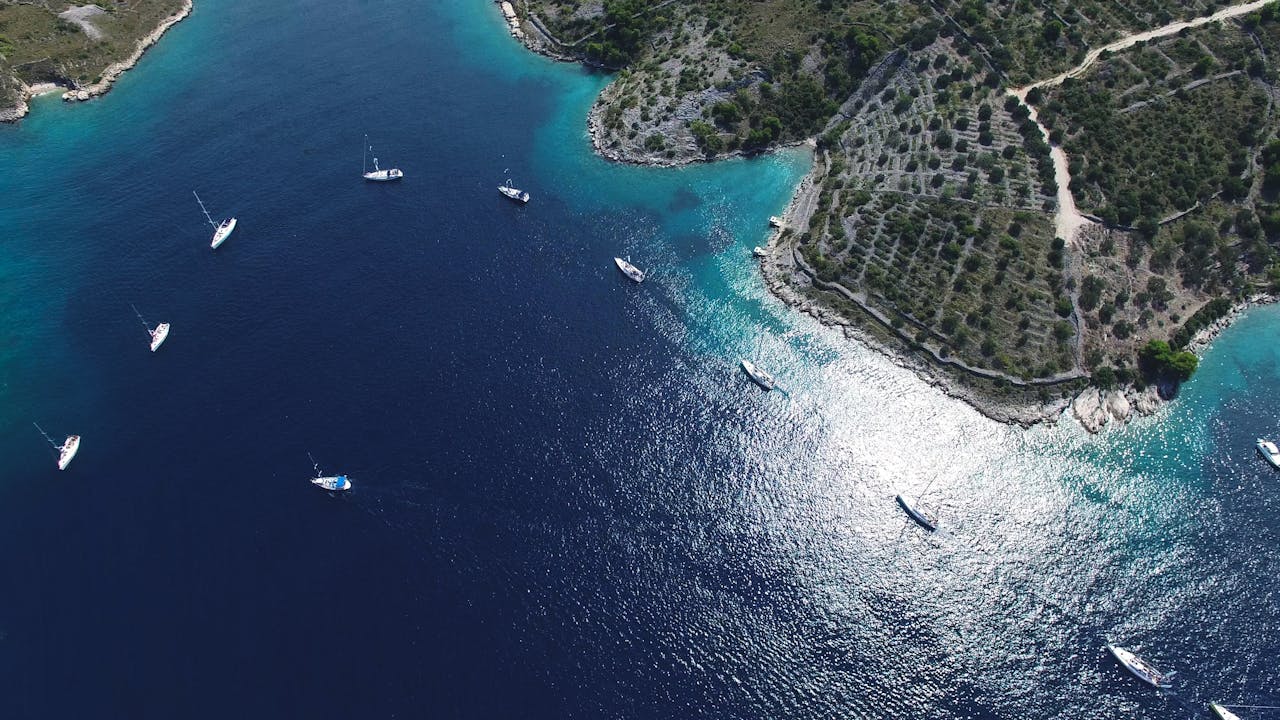 A breathtaking aerial view of sailboats anchored near a lush, rugged coastline with vibrant turquoise waters.
